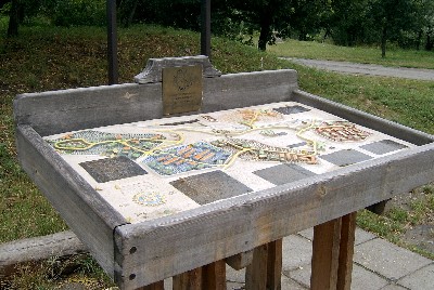 The picture shows the ceramic tactile plan of the entire site, situated at the entrance to the museum. The 3-D buildings stand up from the plan which is appropriately coloured.  The plan is contained in a wooden frame and stand to fit in with its wooded surroundings.