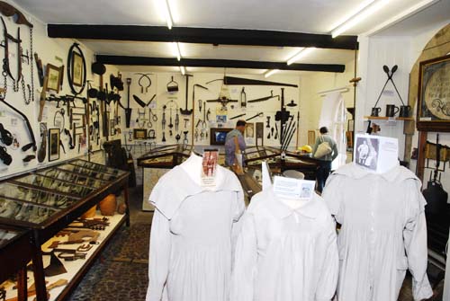 The picture shows the interior of the Museum with show cases and items displayed on the walls. In the foreground are three white linen smocks as worn by farmers in the past. 