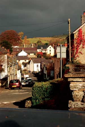 The old houses of the town of Clun go down the hill towards the bridge and the river with a dark winter sky above.