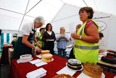 Maggie is standing with a plate, alongside the other judges, waiting to try the next sample of cake