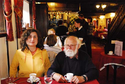 Peter and Maggie are sitting at a table having tea at the famous De Greys cafe. Maggie has shoulder length brown hair and is wearing a yellow jacket. Peter has white hair and a white beard and is wearing a blue jersey. Behind them are the waitresses in their black dresses and white aprons. Peter and Maggie are sitting at a table having tea at the famous De Greys cafe. Maggie has shoulder length brown hair and is wearing a yellow jacket. Peter has white hair and a white beard and is wearing a blue jersey. Behind them are the waitresses in their black dresses and white aprons.