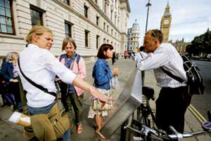 Three women and one man are standing around a long illustrative panel discussing the new design. In the background is the Clock Tower of the Houses of Parliament, better known as Big Ben.