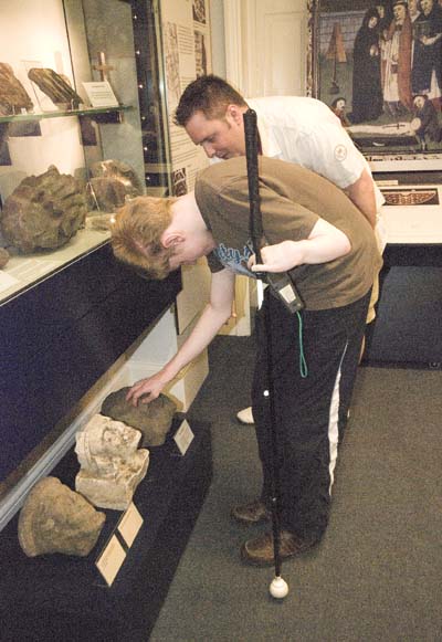 A young man is bending down to touch the stone carvings under one of the display cabinets.