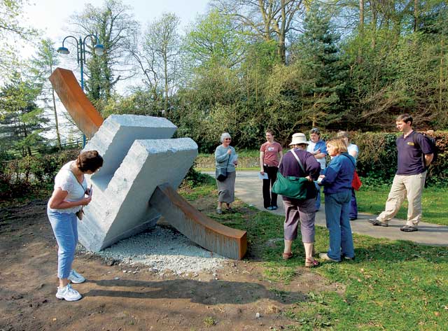 A group is standing around a large white marble block with a steel bar through the middle of it. Trees and the main road at Ellesmere can be seen in the background.
